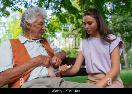 Infermiere che inietta insulina nell'addome di pazienti anziani diabetici. Primo piano di un uomo anziano con diabete di tipo 1 che assume insulazione con l'ago della siringa nel parco Foto Stock