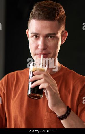 Ritratto di un giovane allegro che sorseggia una bibita analcolica fredda e guarda la macchina fotografica Foto Stock