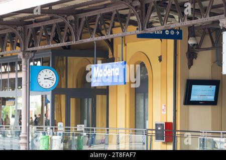 Cartello, orologio e banchina presso la stazione ferroviaria di Modena, Italia Foto Stock