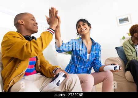 Allegra e diversificata gruppo di amici adolescenti che giocano a videogame a casa Foto Stock