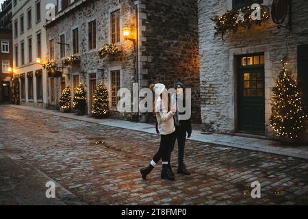 Una coppia romantica che cammina ammirando un albero di Natale splendidamente decorato e una strada illuminata durante il periodo delle vacanze in Quebec, Canada Foto Stock