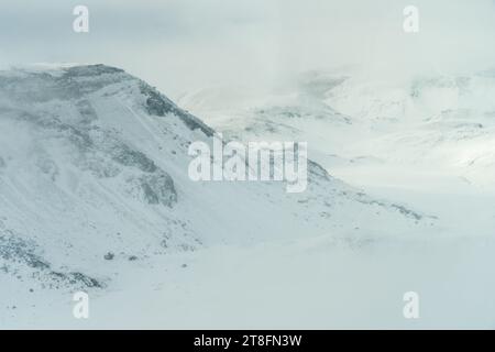 Vista aerea del pendio innevato della montagna, con la soffice foschia che crea un'atmosfera eterea e mascherando i dettagli della vetta lontana Foto Stock