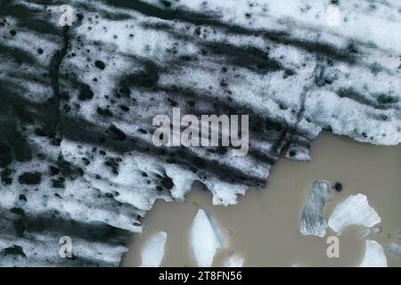 Dall'alto, vista aerea del bordo di un ghiacciaio che scorre nelle acque fangose del mare con iceberg galleggianti nel Parco Nazionale Vatnajokull situato in Islanda Foto Stock