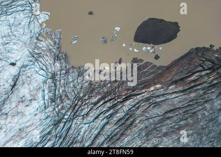 Dall'alto, vista aerea del bordo di un ghiacciaio che scorre nelle acque fangose del mare con iceberg galleggianti nel Parco Nazionale Vatnajokull situato in Islanda Foto Stock