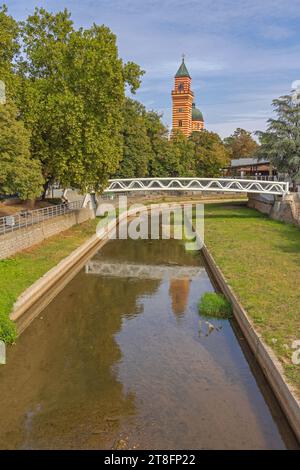 Paracin, Serbia - 06 ottobre 2023: Ponte pedonale sul fiume Crnica e Chiesa della Santissima Trinità nel Parco cittadino in autunno. Foto Stock