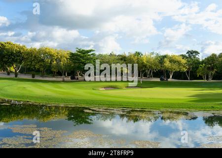 I golfisti sul golf car vicino al green per l'ultimo tiro vicino a un lago in una giornata di sole ai tropici del Messico Foto Stock