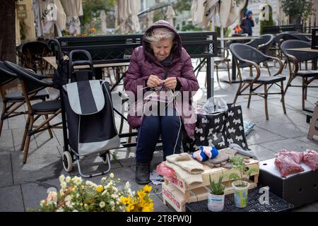 Belgrado, Serbia, 10 novembre 2023: Un'anziana signora vende fiori, guanti e calzini sulla stalla improvvisata mentre si lavora a maglia Foto Stock