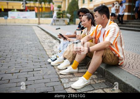 Diversi gruppi di amici seduti sul marciapiede riposano dopo aver camminato per la strada cittadina Foto Stock