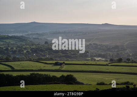 La luce del mattino splende sui terreni agricoli e sui boschi delle valli di Lydford e del Brentor settentrionale sotto le colline e i torti di Dartmoor nel Devon occidentale. Foto Stock