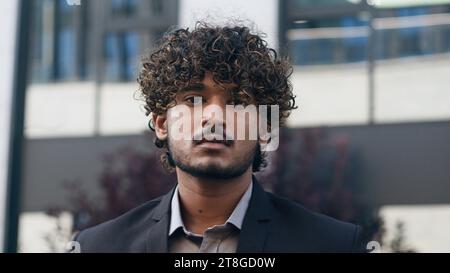 Ritratto di un giovane uomo d'affari indiano arabo che si trova all'aperto in città guardando la macchina fotografica seriamente in città e vicino al business center Foto Stock