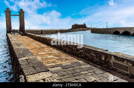 La vista lungo la strada rialzata verso l'isolotto degli inglesi e il Castello di San Gabriele ad Arrecife, Lanzarote in un pomeriggio di sole Foto Stock