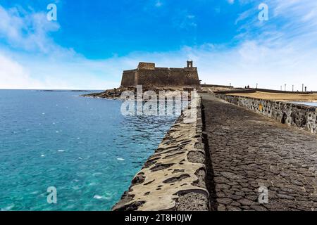 Una vista lungo la strada rialzata verso l'isolotto degli inglesi e il Castello di San Gabriele ad Arrecife, Lanzarote in un pomeriggio di sole Foto Stock