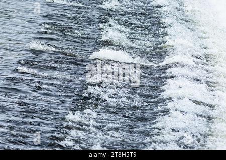 Vista delle acque poco profonde che scorrono sulla diga, creando onde longitudinali. Acqua blu con schiuma bianca. Foto Stock