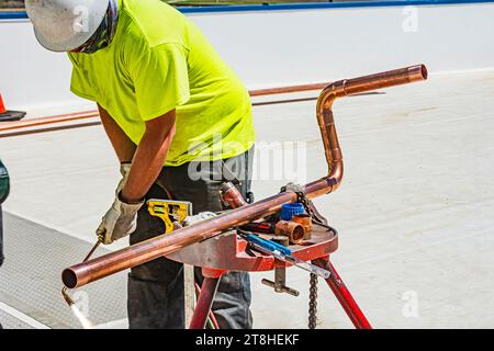 Operaio edile che si prepara a brasare un gomito su una lunghezza di tubo di rame sul tetto in un magazzino di stoccaggio a freddo a CO2 (refrigerazione industriale) Foto Stock