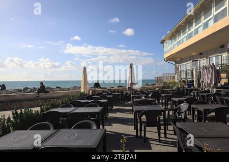 Genova, Italia - novembre 2023 - tavoli e sedie di un ristorante su una passeggiata accanto al frangiflutti in riva al mare Foto Stock