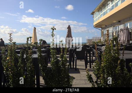 Tavoli e sedie di un ristorante su una passeggiata accanto al frangiflutti in riva al mare Foto Stock