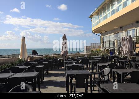 Tavoli e sedie di un ristorante su una passeggiata accanto al frangiflutti in riva al mare Foto Stock