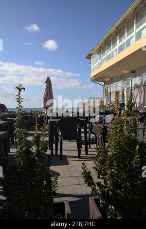 Tavoli e sedie di un ristorante su una passeggiata accanto al frangiflutti in riva al mare Foto Stock