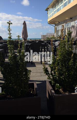 Tavoli e sedie di un ristorante su una passeggiata accanto al frangiflutti in riva al mare Foto Stock