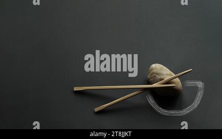 Bacchette di bambù giapponesi e pietra chiara su sfondo grigio scuro. Manipolazione fotografica - silhouette del recipiente disegnata con delicatezza. Spazio copia, minimalismo Foto Stock