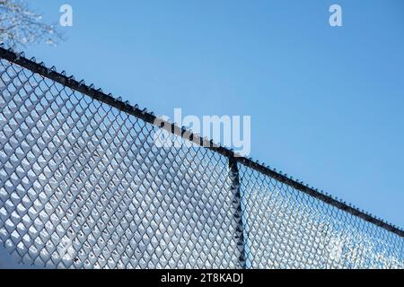 Vista angolare bassa della neve sulla recinzione delle maglie della catena contro il cielo blu Foto Stock