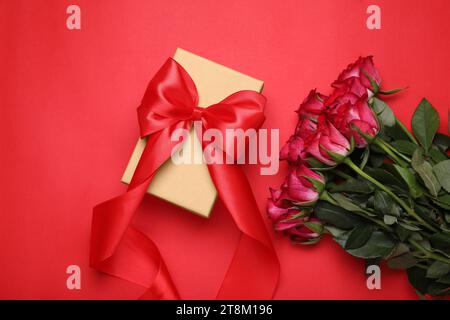 Splendida confezione regalo con fiocco e rose su sfondo rosso, spianata Foto Stock