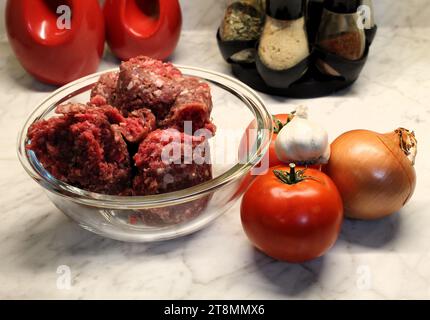 manzo macinato fresco in una ciotola di vetro con verdure e ingredienti da cucina sullo sfondo sul bancone della cucina Foto Stock
