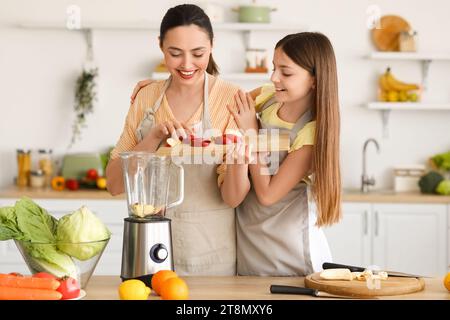 Bambina con la madre che mette la mela tagliata nel frullatore in cucina Foto Stock