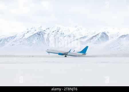 Decollo di un aereo passeggeri in una violenta tempesta di neve sullo sfondo di alte e pittoresche montagne innevate Foto Stock