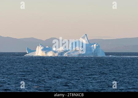 Un iceberg galleggia al sole che sorge al largo delle montagne della costa della Groenlandia. Disko Bay, Groenlandia, Danimarca Foto Stock