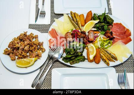 Piatto di appetito su un piatto italiano mediterraneo a tavola fisso Appetiser con piccoli calamari fritti a sinistra, su un grande piatto di prosciutto crudo, formaggio Foto Stock