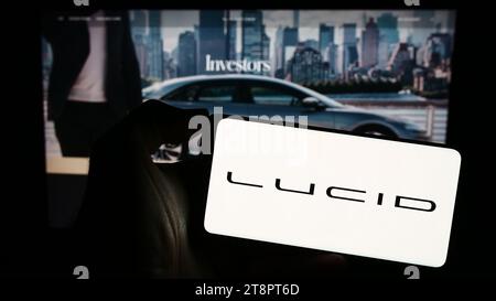 Persona in possesso di un cellulare con il logo dell'azienda statunitense Lucid Motors di veicoli elettrici di lusso davanti alla pagina Web aziendale. Concentrarsi sul display del telefono. Foto Stock