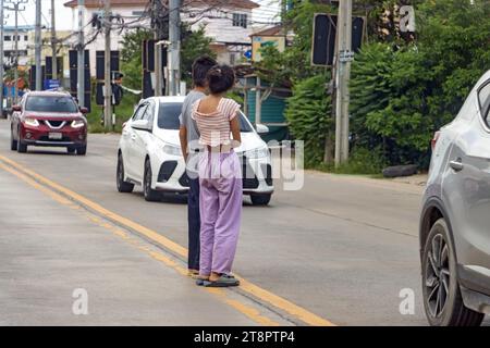 La gente si trova in mezzo alla strada e aspetta di camminare tra le auto in movimento, Bangkok, Thailandia Foto Stock