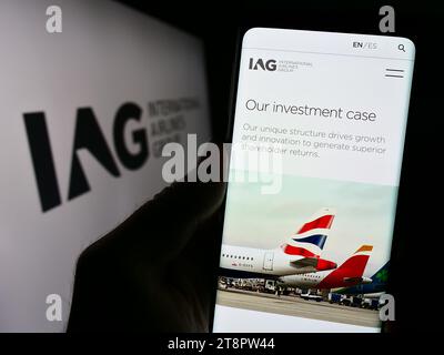 Persona in possesso di cellulare con pagina Web di International Consolidated Airlines Group SA (IAG) davanti al logo. Concentrarsi sul centro del display del telefono. Foto Stock