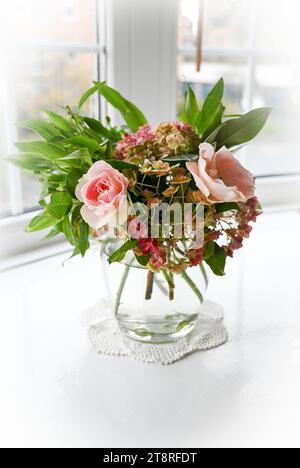 Vaso decorativo di fiori autunnali con rose rosa e fiori di Ortensia in una finestra a bovindo con luce naturale Foto Stock