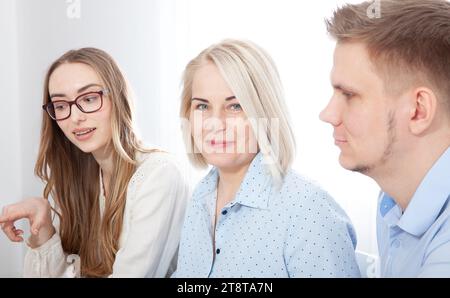 I giovani manager si riuniscono intorno a una donna d'affari esperta in ufficio, impegnata in una conversazione facilitata da un computer portatile. Foto Stock