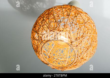 Lampadario moderno con paralume in paglia a forma di sfera appeso sotto il soffitto bianco, foto ravvicinate Foto Stock