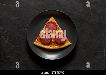 Pizzeria con peperoni, un pezzo triangolare su un piatto rotondo grigio, su sfondo scuro, vista dall'alto, spazio per copiare il testo. Foto Stock