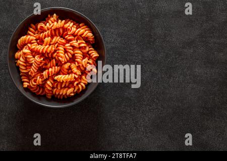 Fusilli, pasta cotta con salsa di pomodoro, su sfondo scuro, vista dall'alto, spazio per copiare il testo. Foto Stock