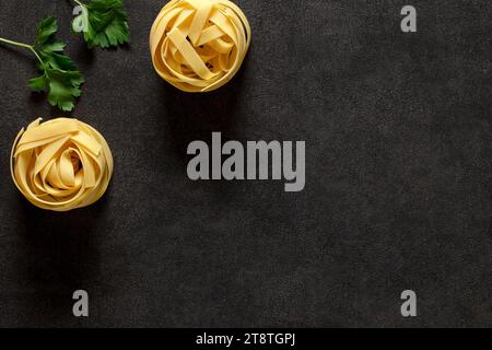 Fettuccine, due nidi crudi crudi e prezzemolo - ingredienti per un piatto italiano, su sfondo scuro, vista dall'alto, spazio per copiare il testo. Foto Stock