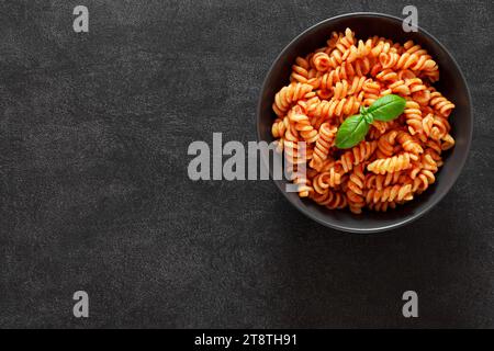 Fusilli cotti con salsa di pomodori e basilico su sfondo scuro, vista dall'alto, spazio per copiare il testo. Foto Stock