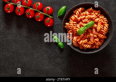 Fusilli, pasta cotta con salsa di pomodoro, ciliegia di pomodoro e foglia di basilico, su sfondo scuro, vista dall'alto, spazio per copiare il testo. Foto Stock