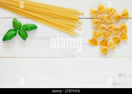 Fusilli, spaghetti, pasta cruda, foglia di basilico su fondo di legno bianco, vista dall'alto, spazio per copiare il testo. Foto Stock