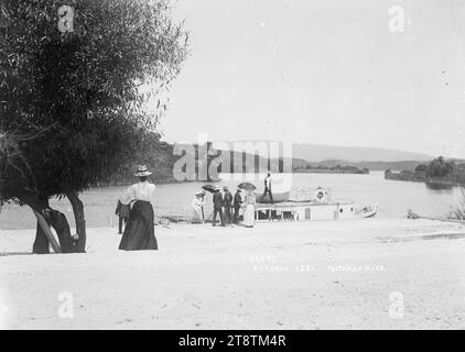 Traghetti e turisti a Okere sul lago Rotoiti, turisti che sbarcano da un traghetto al molo di Okere sul lago Rotoiti. Due delle donne tengono in mano degli ombrelloni per tenersi in ombra dal sole. CA 1908 dal litorale guardando dall'altra parte dell'insenatura di Okere al lago Rotoiti in lontananza Foto Stock