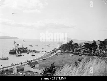 Il traghetto a Bucklands Beach, Auckland, nuova Zelanda, Una vista di Bucklands Beach, Auckland, nuova Zelanda, in un giorno d'estate con il traghetto al molo in attesa di portare i passeggeri attraverso Auckland, nuova Zelanda. Le imbarcazioni da diporto sono ancorate vicino alla spiaggia e piccole barche a vela circondano il traghetto. Un grande gruppo di persone può essere visto tra gli alberi a destra. L'isola di Rangitoto è in lontananza all'inizio degli anni '1900 Foto Stock