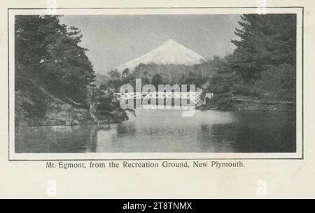 Cartolina. Monte Egmont, dal Recreation Ground, New Plymouth. 1900-1920, mostra un Monte Taranaki innevato visto da un lago o da un fiume, con un ponte dipinto di bianco in primo piano Foto Stock