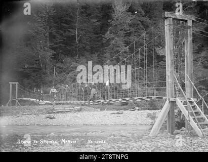 Altalena il ponte sul fiume Maruia che conduce alle sorgenti di Maruia, veduta di un gruppo di uomini in piedi sul ponte sospeso sul fiume Maruia, che conduce alle sorgenti di Maruia. ca 1910 Foto Stock