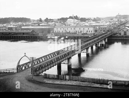 Vista di Wanganui, nuova Zelanda con il Ponte cittadino che si estende sul fiume Whanganui in primo piano, Vista di Wanganui, nuova Zelanda attraverso il fiume Whanganui. Cobham Bridge è in primo piano, con le sedi aziendali di M. Hogan & Company Ltd, H.I. Jones & Sons Ltd, e la filiale neozelandese di Wanganui, della New Zealand Loan & Mercantile Agency Company, sull'altra sponda del fiume Foto Stock