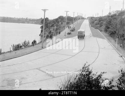 Strada principale da Northcote Wharf, Auckland, nuova Zelanda, vista su Queen Street dal Northcote Wharf End, mostra un autobus che viaggia lontano dal molo, e una moto e un'auto parcheggiate sul lato della strada. Diverse persone possono essere viste camminare sul sentiero accanto alla strada di cemento. Little Shoal Bay può essere vista sul lato destro. ca 1920 Foto Stock