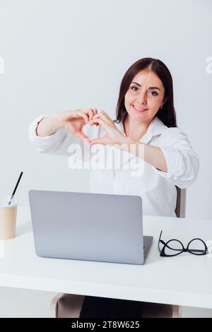 Donna d'affari che mostra il cuore delle mani in ufficio Foto Stock